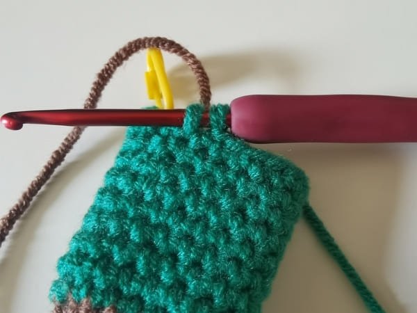 put the brown yarn behind two dark green loops